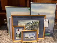Group photo showing five framed watercolor paintings with coastal and nature scenes. Various frame sizes and colors visible including light wood and lavender mats.