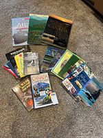 Photo showing assortment of approximately 15 books with Canada and British Columbia themes laid out on carpet, along with two small binoculars.