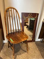 Wooden chair with curved vertical backrest next to wood-framed mirror with gold embellishments on frame edges