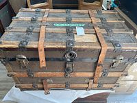 Front view of the vintage trunk showing leather straps, metal corner reinforcements and central lock.