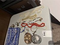 Multiple necklaces, fabric jewelry roll, shell mosaic and silver-tone trinket boxes on table