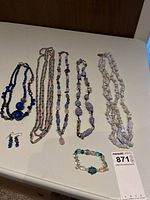 Photo of six necklaces, one pair of earrings, and one bracelet arranged on a white surface