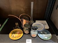 All items arranged on shelf including decorative plates, pottery pieces, copper jug, coasters, and glass candlestick