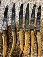 Close-up image of 6 vintage serrated knives with wood-textured handles shaped like antlers.