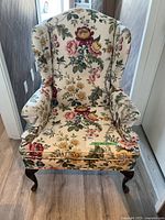 Front view of floral wingback chair showing upholstery pattern and wooden legs.