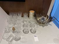 Full lot overview showing wine glasses, dessert glasses, salt and pepper shakers, decorative glass bowl, and additional pieces on a white tabletop with wooden background.