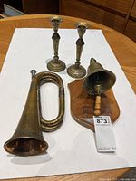 Photo showing the vintage metal horn, pair of metal candle holders, and mounted bell on a table.