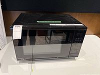 Front angled view of black Panasonic microwave oven on white surface showing door and control panel area.