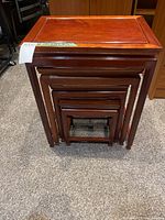 Set of four nested reddish-brown wooden tables from front showing size gradation and nesting.