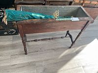Wooden planter box seen from an angle showing the wood structure and metal tray inside, placed on a floor.