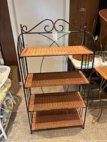 Front view of rattan shelf unit on wrought iron frame with four shelves.