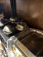 Photo of silver tone serving dishes with lids, butter dishes, and trays showing tarnish and wear.