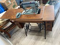 Full view of the wooden Singer sewing table with attached Ford de luxe sewing machine and fold-out wooden extension panel.