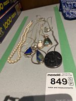 All five necklaces displayed together on a tabletop, showing the pearl strand and four silver chains with various pendants.