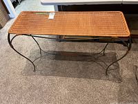 Top-down angled view of the rectangular rattan table on wrought iron legs, shown on carpet.