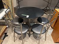 Full view of round black table with four matching metal chairs around it.