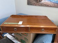 Wooden table top chest showing two drawers with brass ring handles and overall top view.