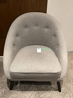 Grey fabric tub chair front view showing curved and button tufted backrest and cushioned seat.