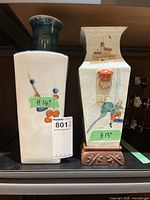 Two Asian themed porcelain vases side by side, showing height markers of 14 and 13 inches, placed on a shelf.