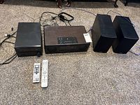 Wide angle photo of the Yamaha radio system, separate CD player, two speakers and remotes laid on carpet.