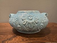 Photo showing front of blue ceramic vase with embossed floral and geometric design and loop handles.