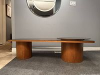 Front view of entire coffee table showing curved wood veneer top, two cylindrical bases and smoked glass top.