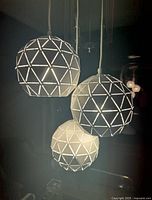 Three hanging spherical metal ball light fixtures with triangular geometric cutouts lit up, showing the lattice pattern glowing.