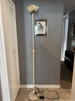 Full view of tall postmodern floor lamp with cream pole and base, standing against a gray wall