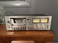 Front view of Toshiba stereo cassette deck player model PC-3460 on a wooden surface showing cassette compartment, control buttons, knobs, headphone jack, and VU meters.