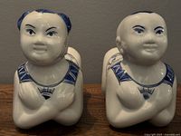Close-up of the two ceramic boy figures side by side showing detailed facial features and cross-armed pose, glossy finish, no visible damage.