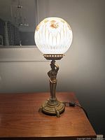 Full side view of vintage Art Deco lamp showing bronze-tone figure base and globular frosted glass shade with floral decoration.