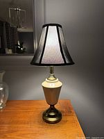 Full view of vintage ceramic and brass table lamp with black-bordered light fabric shade on wooden surface