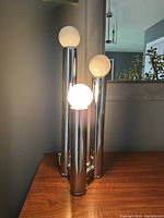 Front view of lamp lit showing three chrome cylinders with globe bulbs