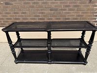 Front view showing the black finish, turned legs, and caned surfaces on the upper two tiers of the console table.