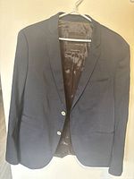 Front view of black Zara men's blazer on white hanger showing notch lapels, two buttons, chest pocket, and two front flap pockets with fully lined interior.