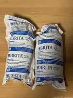 Four sealed Brita pitch water filter cartridges on wooden surface with branded packaging visible
