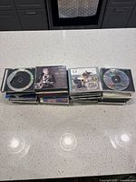 View of two stacks of old CDs in jewel cases on a kitchen counter showing front and back covers.