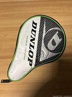 White paddle cover with Dunlop branding and green trim, shown on wooden surface.