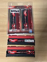 Four G Skill Trident X DDR3 RAM sticks displayed with two out of package and two sealed in original blister packaging, showing red and black heat spreaders and gold connectors.