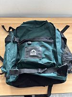 Front view of green and black hiking backpack showing main and front compartments, side mesh pocket, and adjustable straps.