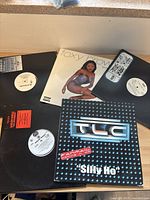Six hip hop vinyl record singles displayed on a surface, including TLC "Silly Ho" and Foxy Brown records.