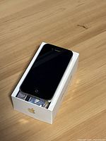 Front view of the Apple iPhone 4s showing intact screen and home button placed on original white Apple box.