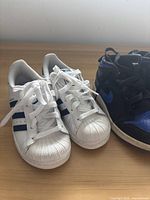 Pair of white Adidas kid's sneakers showing side and front with blue stripes and shell toe detail