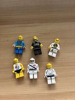 Photo showing six LEGO minifigures with various outfits and yellow heads and hands laid on a wooden surface.