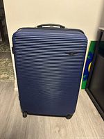 Full front view of the dark blue luggage suitcase showing ridged hard shell and spinner wheels.