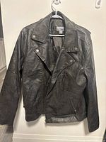Front view of black men's faux leather jacket on hanger, showing biker style with lapel collar, silver metal snap details, and side zipper pockets.
