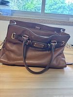 Brown Michael Kors leather handbag with dual straps, placed on a wooden surface in front of a window