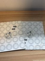 Two white vinyl record sleeves with circular logo pattern and accompanying vinyl discs placed on wooden surface.