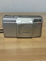 Front view of the Olympus Super Zoom 80G camera with lens cover closed, showing silver body and flash.