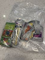 A large quantity of assorted Pokémon cards within a clear plastic bag placed on a countertop. Mixed card types and conditions.